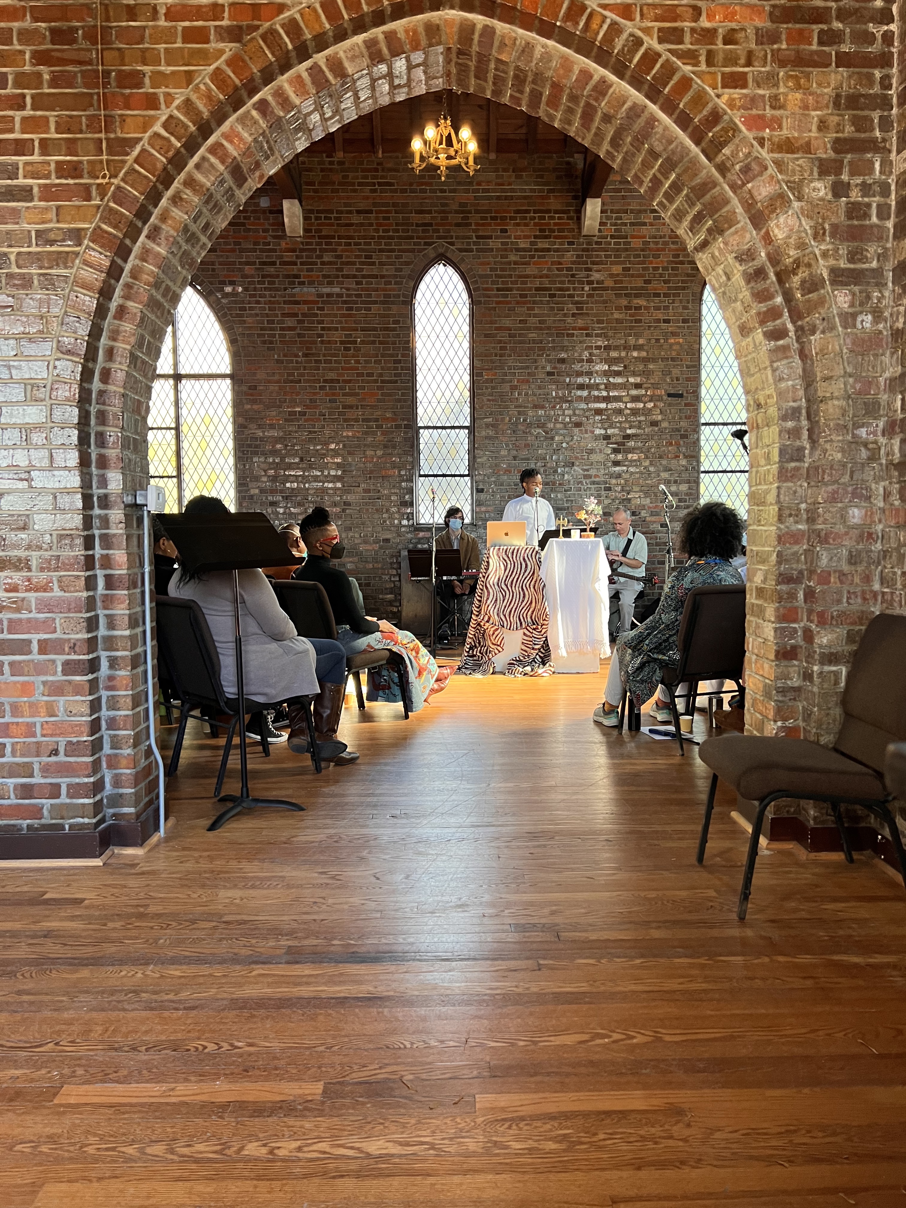 Sangodare standing at African print covered photo framed by archway with congregation and band surrounding